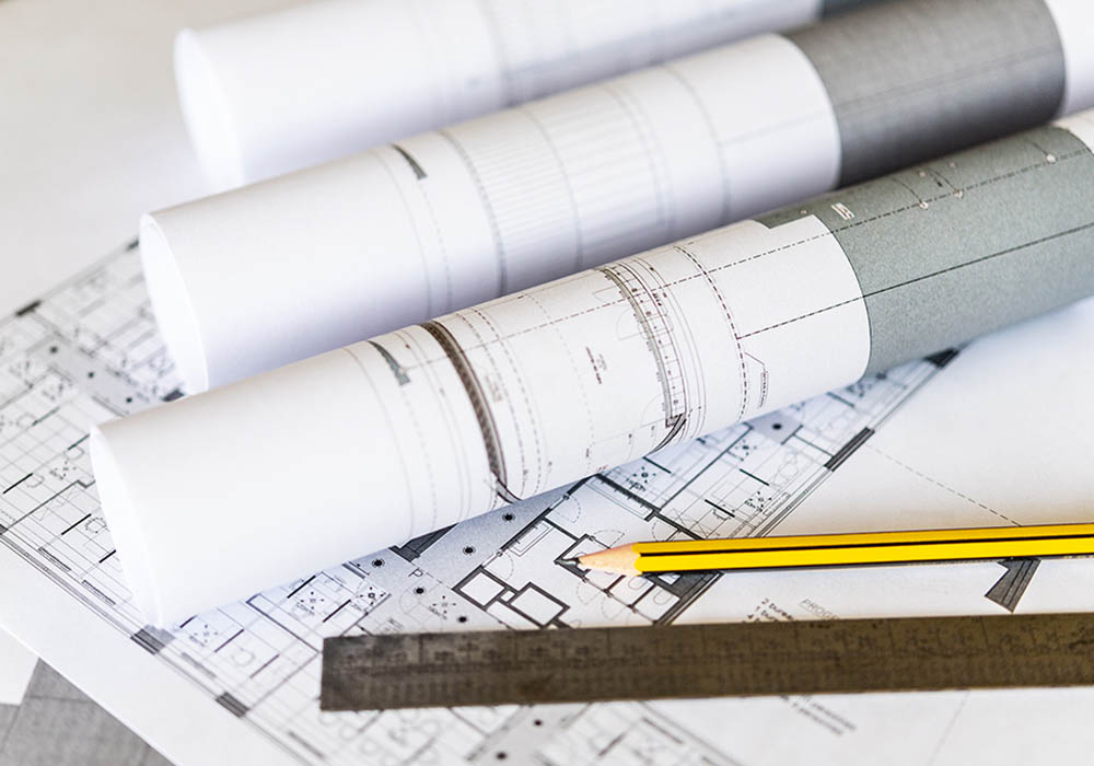 Architecte sur chantier chemise jeans crayon tablette mac book pro plan de maison calculatrice tasse de café ouvrier casque de chantier jaune chemise foncée tient porte document avec copie de plan pour travailler